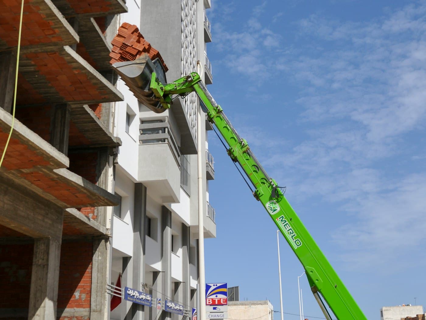 A telehandler lifting a banded pallet of brick at a building site.